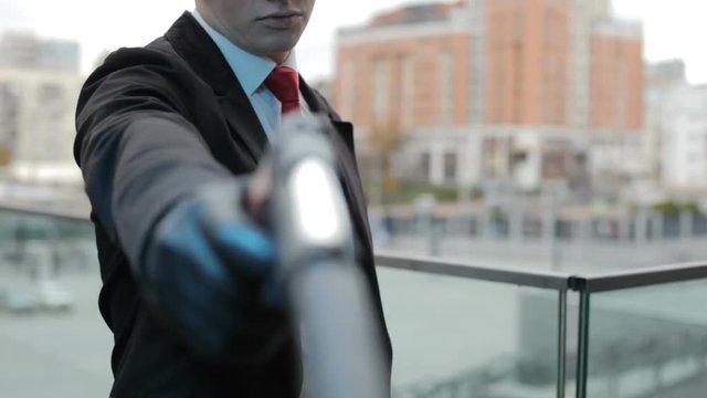 Hitman nervously taps the pistol on his arm in black gloves.