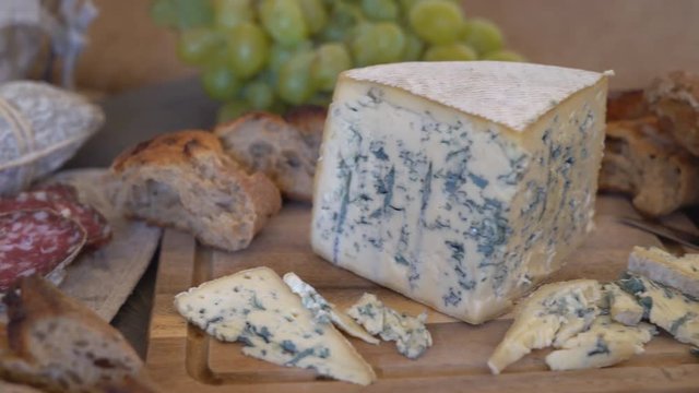 appetizing sausage loaf in a bag of marble fabric. the sausage rests on a wooden table of brown color. In the background a baguette, cheese with green mold and a large bunch of white grapes with a