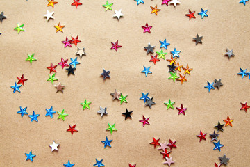 Holiday background with little multicolored crystal stars on craft paper.