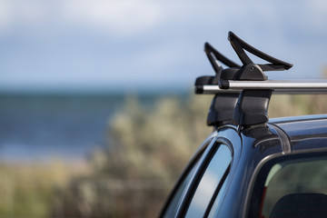 Car with kayak holders on roofracks with the ocean in the background. The ocean is calm and the sky has some clouds.