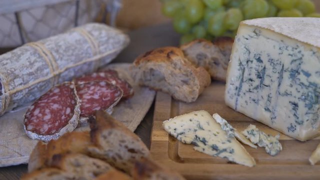 appetizing sausage loaf in a bag of marble fabric. the sausage rests on a wooden table of brown color. In the background a baguette, cheese with green mold and a large bunch of white grapes with a