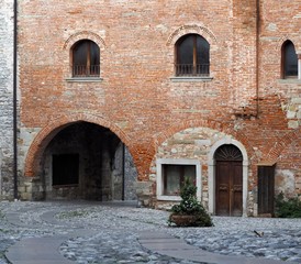 Fototapeta na wymiar Medieval street arch under an ancient brick wall of a building facade in the town of Cividale del Friuli, now in italy