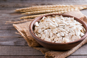 Dried pumpkin seeds in bowl on wooden background