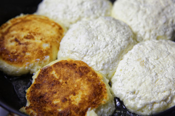 Homemade cheese pancakes or syrniki are fried in a frying pan. Traditional rustic food in Russian, Belarusian, Latvian, Lithuanian, Serbian and Ukrainian cuisines.