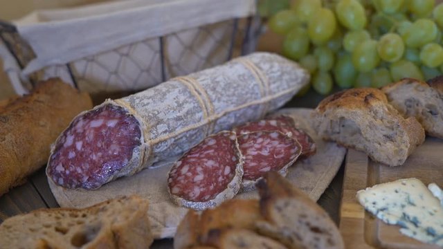 appetizing sausage loaf in a bag of marble fabric. the sausage rests on a wooden table of brown color. In the background a baguette, cheese with green mold and a large bunch of white grapes with a