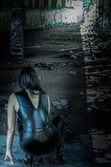 Frau kniet in Catsuit bei Lost Place, Abendstimmung