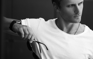 Street fashion concept. Portrait of a young and handsome man in a white t shirt and trendy glasses posing over black modern background. Close up. Street shot. copy space