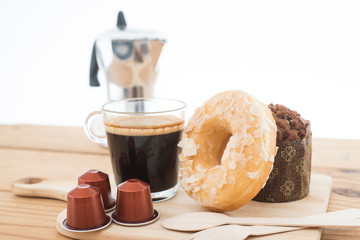 Cup of espresso, espresso capsule and bakery on wooden table.