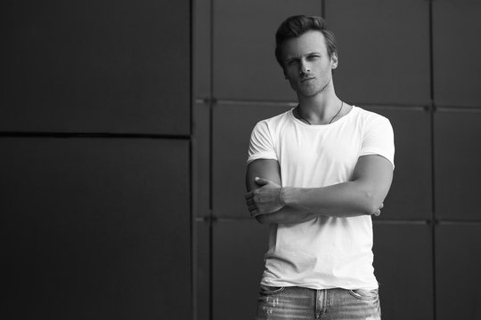 Street fashion concept. Portrait of a young and handsome man in a white t shirt and trendy jeans, posing over black modern background. Close up. Street shot. copy space