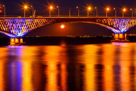Bright night lights of a large bridge across the river are refle