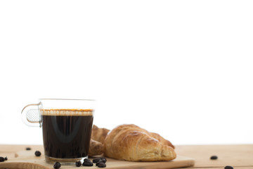 Cup of espresso and croissant on wooden table.