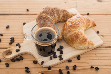 Cup of espresso and croissant on wooden table.