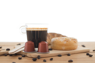 Cup of espresso, espresso capsule and bakery on wooden table.