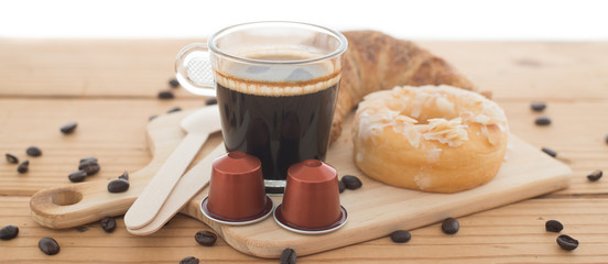 Cup of espresso, espresso capsule and bakery on wooden table.