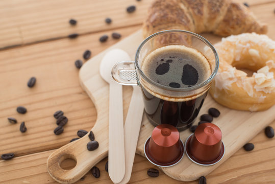 Cup of espresso, espresso capsule and bakery on wooden table.