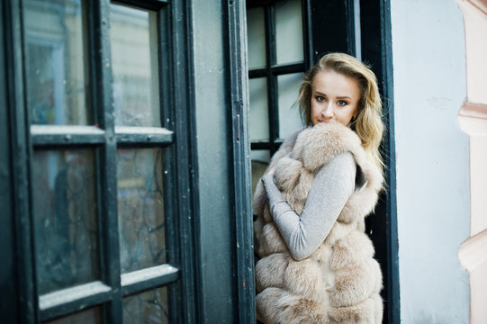 Blonde girl at fur coat posed against old wooden door.
