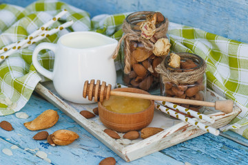 Honey in the wooden bowl, almonds and jar with milk on the wooden tray