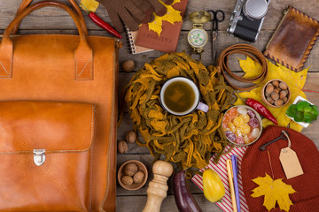 The concept of autumn travel - a cup of tea, vegetables, maple leaves, camera, compass, passport, key with blank label, belt, a purse, warm clothes: a hat, scarf and gloves