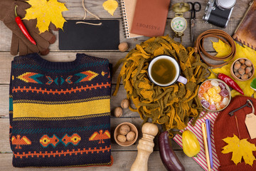 The concept of autumn travel - a cup of tea, vegetables, blank blackboard, maple leaves, camera, compass, passport, scissors, key with blank label, warm clothes: a hat, scarf, pullover and gloves
