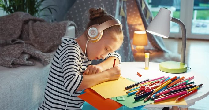 Child girl writing in greeting card and listening music in headphones