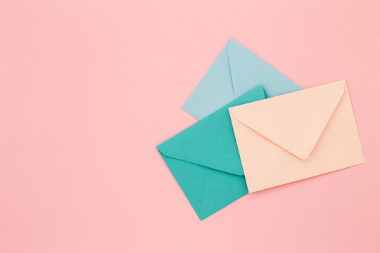 Three colored envelopes on pink background. Minimalist styled composition, top view, correspondence concept.