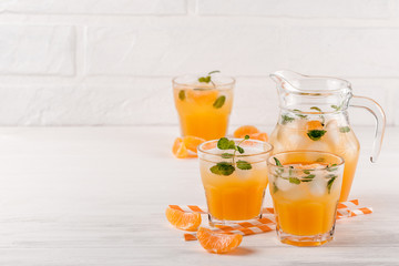 Mandarin cocktail with ice and mint in beautiful glasses and jug, fresh ripe citrus on white wooden background. Sweet orange juice. Close up photography. Selective focus