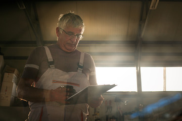 Senior man in workshop. Man writing in his planner book.