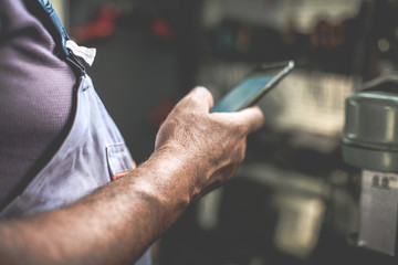 Senior man in workshop. Man holding mobile and reading text. Close up.