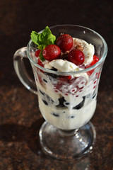 Christmas dessert. Perfect combination of vanilla ice cream, red and black currant, cranberry, mint and winter spices. Sweet winter treat in a glass cup for cappuccino on dark background.