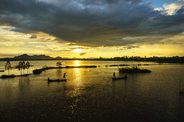Naklejka premium Sunset on cultivated field with fishermen catching fish by throwing nest in An Giang, south of Vietnam