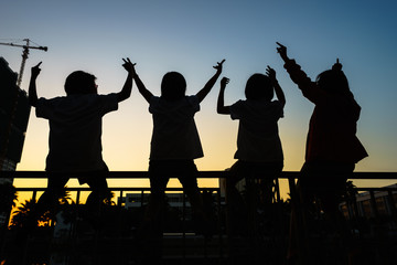 Group of happy children raising hands at summer sunset