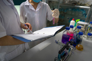 Asian female scientist writing down notes and test report from research with test tubes in...