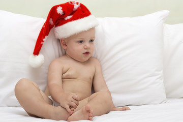 Picture of cute baby wearing santa hat while lying on the bed, on white background