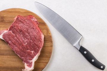 Raw beef steak on the white marble table with chef knife in the background