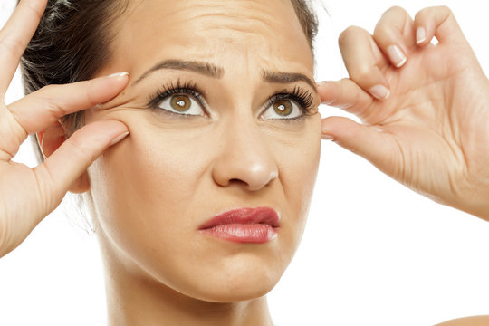 young women pinching her wrinkles  next to her eyes with her fingers