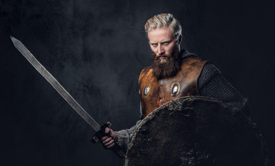 Viking dressed in Nordic armor holds a shield and silver sword.