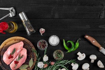 Raw chicken breast fillets on wooden cutting board with herbs, spices, mushrooms and chili peppers. Top view with copy space