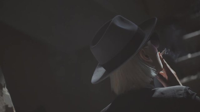 A beautiful girl in black clothes and a hat, walking along an old collapsed building. The girl in a hat smokes