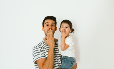 Naklejka premium Father and beautiful little daughter shocked, isolated over a white background. Parenthood and childhood. Surprised dad and his toddler girl close mouth with hand. Lifestyle of happy family.