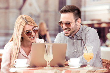 Happy couple at coffee shop looking at laptop.