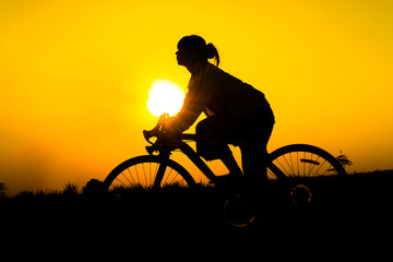 Silhouette of young woman cyclist on sunset sky with riding along the prairie at yellow evening horizon sea yellow sunset heaven background outdoor.