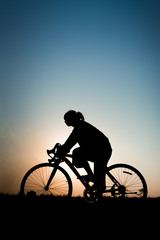 Silhouette of young woman with bicycle on sunset.