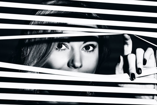 Closeup shot of sexy young woman looks through the jalousie