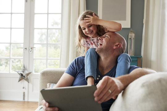 Father using digital tablet while daughter sitting on his shoulder at home