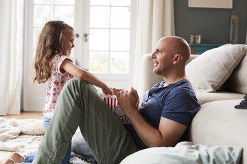 Side view of smiling father and daughter eating popcorn at home
