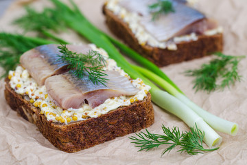 Herring, green onions, butter, French mustard and a slice of rye bread on an old wooden table.