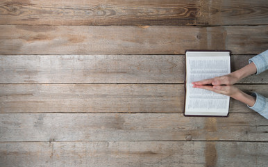 Woman hands holding a bible over a desk. She is reading and paying. Overhead point of view