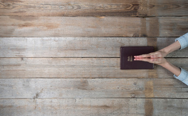 Woman hands holding a bible over a desk. She is reading and paying. Overhead point of view