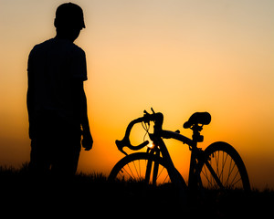 Obraz premium A silhouette of a person standing next to a bicycle in front of an orange sunset.