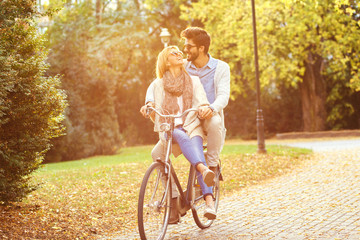 Happy young couple having fun riding a bicycle on sunny autumn day in the park.	